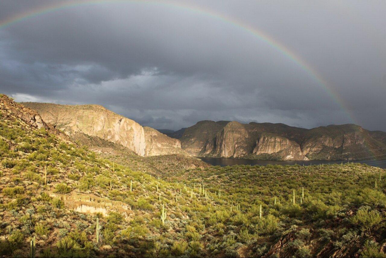Rainbow over Canyon Lake and its canyon walls after a desert storm, with green saguaro-covered hills